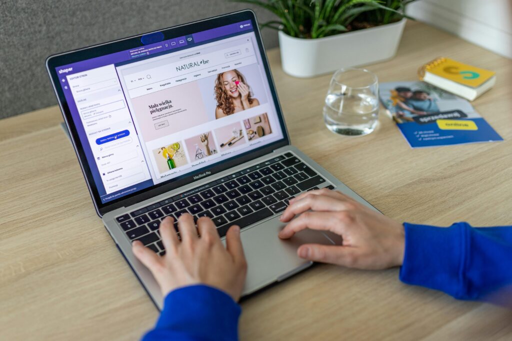 Hands typing on a laptop showing an e-commerce website in a modern office setting.