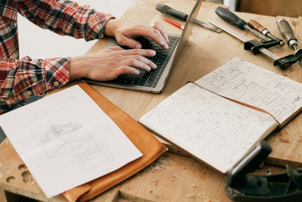 A woodworker uses a laptop to design furniture in a workshop setting, highlighting the blend of technology and craftsmanship.