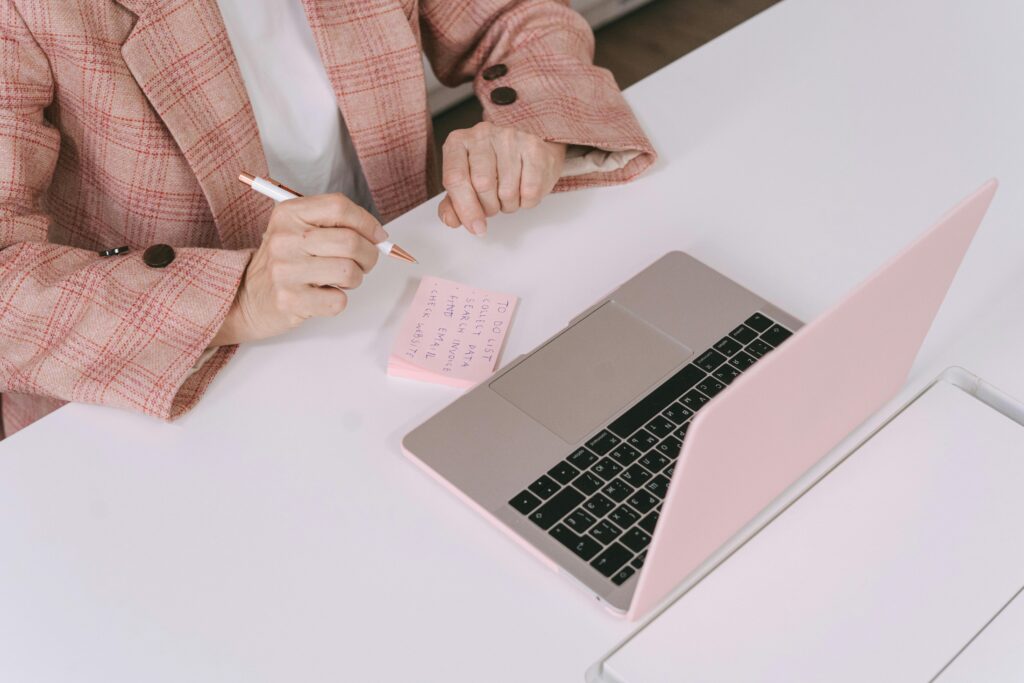 Businesswoman in a plaid jacket using a laptop and sticky notes for work planning.