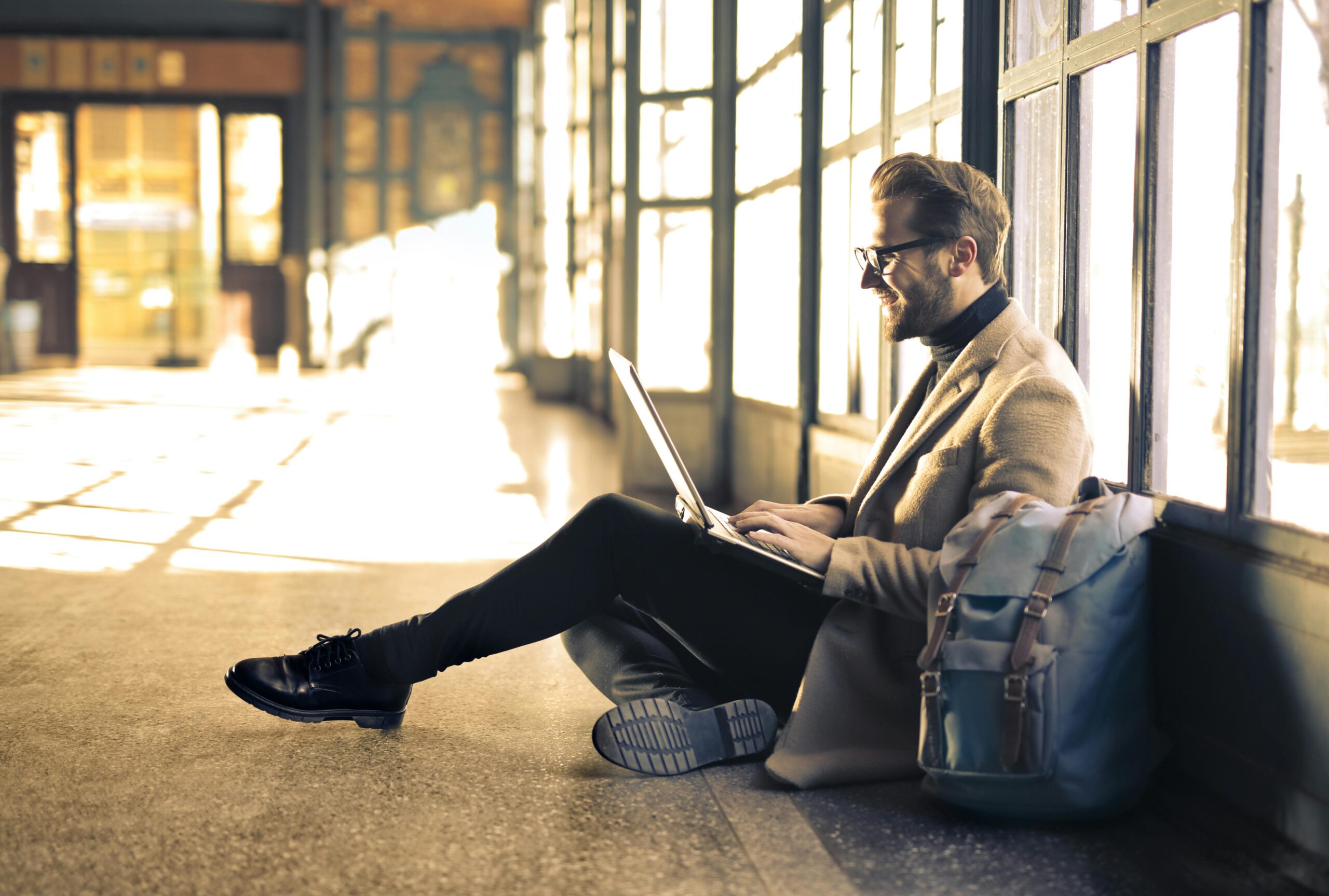 Man sitting by a window at a Budapest train station, working on his laptop with sunlight streaming through.